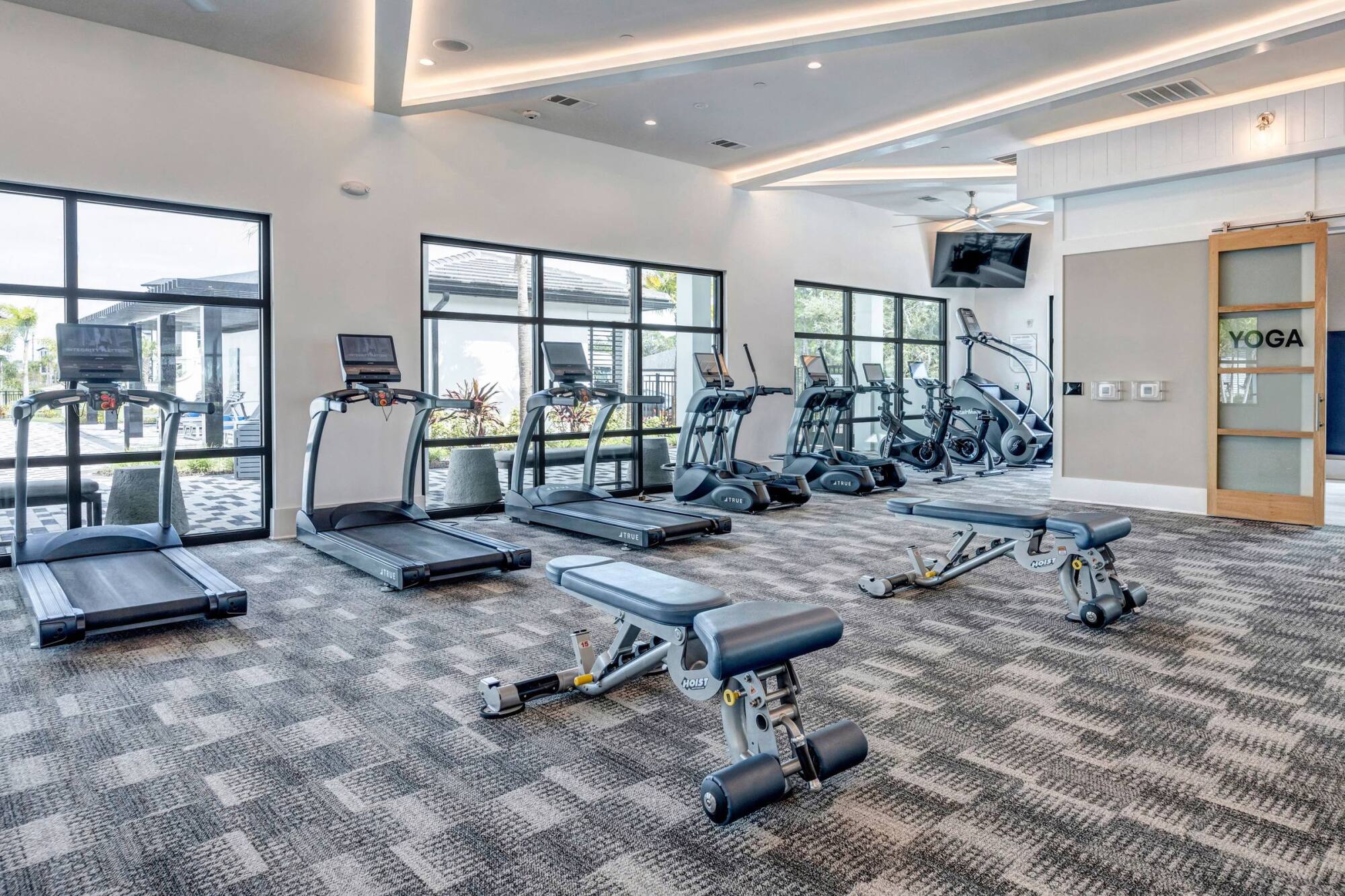 Fitness center at Avasa Hammock Landing in West Melbourne, FL with treadmills, ellipticals, and training benches by floor-to-ceiling windows.