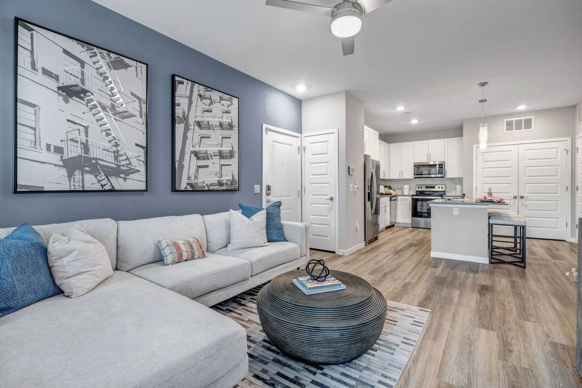 Apartment living room at Avasa Hammock Landing in West Melbourne, FL with a sectional sofa, blue accent wall, and wood-plank flooring.