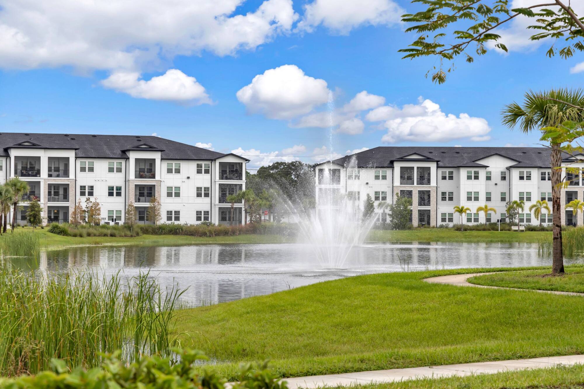 Apartment buildings at Avasa Hammock Landing in West Melbourne, FL overlooking a lake with a fountain and open lawn.